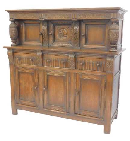 A 20thC oak court cupboard, the top with a moulded edge above a carved section above three panelled doors, the central door with a carved male in profile, with leaf carved columns to each side, the base with three panelled drawers, on stiles, 148cm high, 