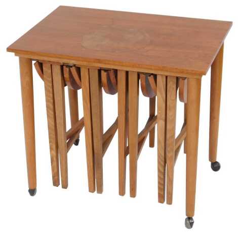 A mid century teak nest of tables, rectangular top raised on cylindrical tapering legs, on castors, enclosing four smaller drop leaf tables, 56cm high, the top 62cm x 42cm of the largest.