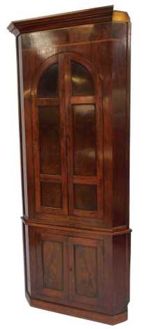 An early 19thC mahogany and banded corner cupboard, the out swept pediment over a pair of doors, opening to reveal three shaped shelves, above two further cupboard doors, raised on a plinth base, 222cm high, 90cm wide, 52cm deep.