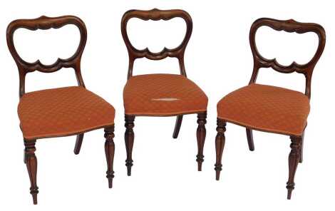 A set of three Victorian mahogany dining chairs, each with a shaped balloon back, overstuffed seat, on cylindrical fluted legs.