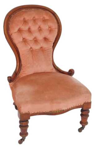 A Victorian mahogany framed nursing chair, with spoon pink upholstered button back, overstuffed seat, on cylindrical turned legs with castors.