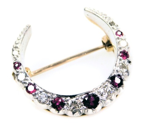 A ruby and diamond crescent moon shaped brooch, set with seven rubies, and eight diamonds at intervals, in white and yellow metal, 4.6g.