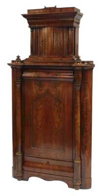 An early Victorian flame mahogany corner cupboard, with a shaped pediment over a serpentine door, flanked by turned columns, over a cushion drawer, panelled door enclosing two shelves, and further cushion drawer, flanked by turned columns, raised on a pli