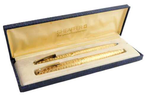 A Sheaffer pen set, comprising a fountain pen with 14ct nib and a ballpoint pen, each in gold coloured casing with a ribbed decoration, boxed.