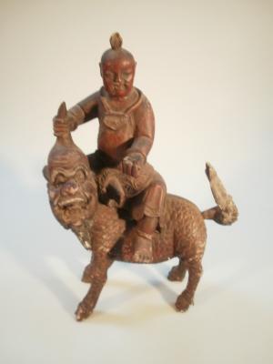 A Chinese hardwood figure of a deity astride a Shi-Shi