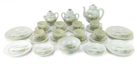 A 20thC Japanese eggshell porcelain tea set, comprising teapot, milk jug, sugar bowl, eight cups and saucers, four medium plates and a bowl, each decorated with buildings, mountains and trees, on a white ground.