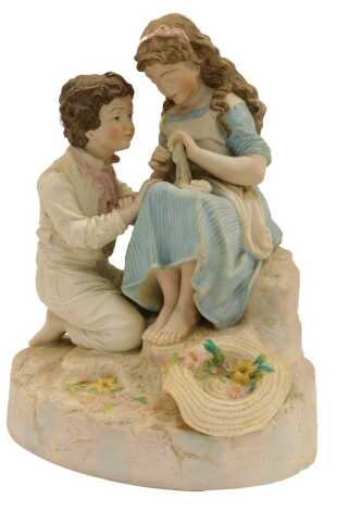 A 20thC bisque figure group, depicting a young girl seated holding fabric beside a kneeling boy, 37cm high.