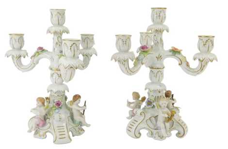 A pair of 20thC Schierholz porcelain candelabra, with floral encrusted decoration with three seated cherubs to each base holding musical instruments, gilt heightened, printed marks, 31cm high. (AF)