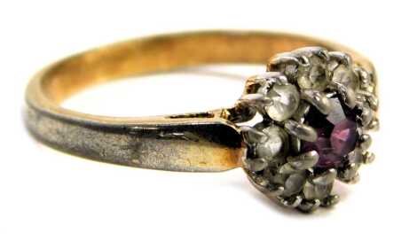 A fashion ring, the floral cluster central set with purple stone, surrounded by paste stones, on silver collared base metal band, ring size N½.