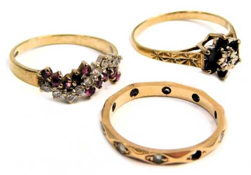 Three dress rings, comprising a 9ct gold half hoop dress ring, of twist design, set with garnets and czs, ring size K½, sapphire and diamond cluster ring, ring size L, and an eternity ring set with cz stones, yellow metal unmarked, ring size M½, 4.2g all