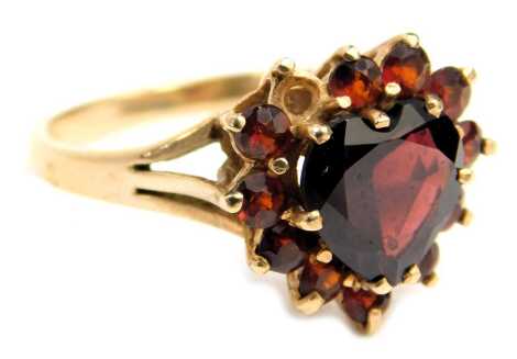 A 9ct gold garnet cluster ring, the central heart shaped garnet surrounded by round brilliant cut stones, each claw set with V splayed shoulders, in a raised basket, one stone missing, ring size N, 2.8g all in.