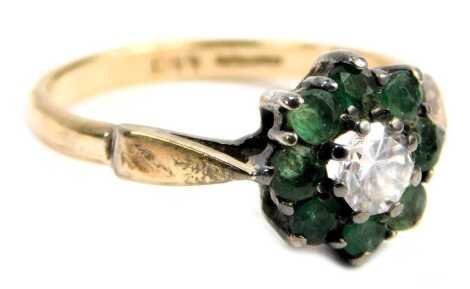 An emerald and paste stone set floral cluster ring, in a raised basket, the yellow metal band hallmarked silver and marked 9ct, ring size N, 1.9g all in.