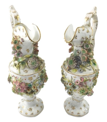 A pair of 19thC porcelain ewers, each with raised flower encrusted decoration, within gilt borders, unmarked, 33cm high. (AF)