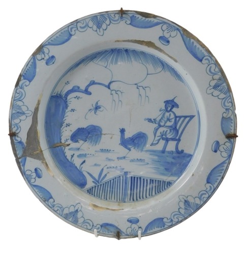 An 18thC Delft charger, decorated in Oriental style, with a seated man smoking, beside cockerels, a fence, etc., 36cm diameter. (AF)