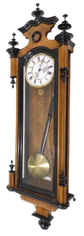 A walnut and ebonised Vienna wall clock, the shaped crest with turned finials, the enamel type dial with Roman numerals, 124cm long.