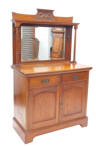 A late 19thC/early 20thC oak sideboard, the mirror back with carved Art Nouveau motifs of flowers, and a rectangular bevelled plate, on turned supports, the base with two drawers and two doors with arched panels, on bracket feet, 106cm wide.