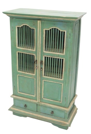 A green and cream painted Eastern cabinet, the two doors with cylindrical grills and two square panels, above two drawers, on bracket feet, 111cm high, 69cm wide.