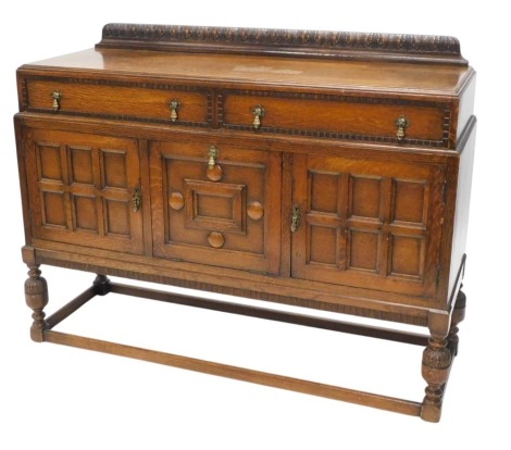 An early to mid 20thC oak sideboard, with leaf carved raised back above two frieze drawers, three panelled doors, each with teardrop shaped brass handles, on cup and cover supports, with stretchers, 146cm wide.