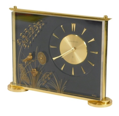 A Jaeger-LeCoultre Marina desk clock, with a black and gilt decoration of floral sprays and birds, with Swiss eight day movement on circular foot, 16cm high, 21cm wide.