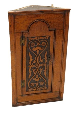 An oak hanging corner cabinet, the single carved door with brass H hinges, 89cm high, 50cm deep.