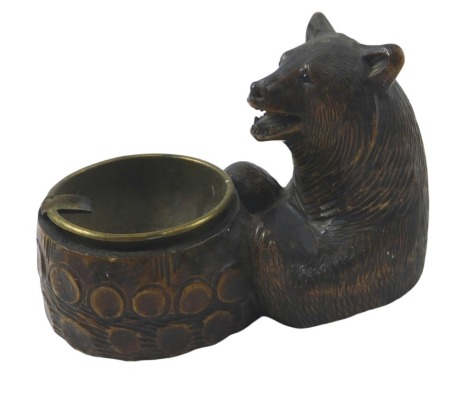 A Black Forest ashtray, carved in the form of a bear, with brass insert, 16cm long.