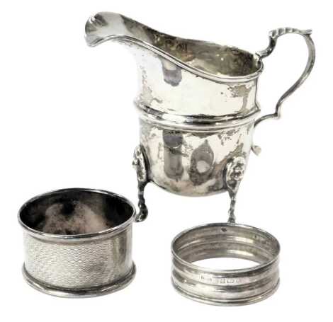 A George V silver milk jug, with moulded thumb piece, on tripod twist stem lion mask feet, Birmingham 1920, and two later silver napkin rings, 2.79oz. (3)