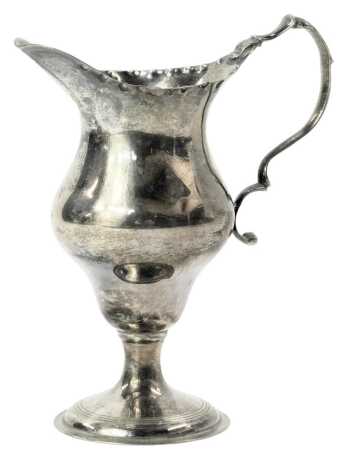 A George V silver pedestal cream jug, with a hammered border and acanthus leaf moulded handle, on circular foot, maker R&K, London 1929, 2.53oz.