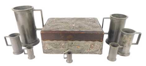 An Arts & Crafts pewter mounted wooden workbox, the lid repousee decorated and glass jewel inset with flowers, the sides with fish and seaweed, 27cm wide, together with a graduated set of pewter measures or tankards, the largest 19cm high.