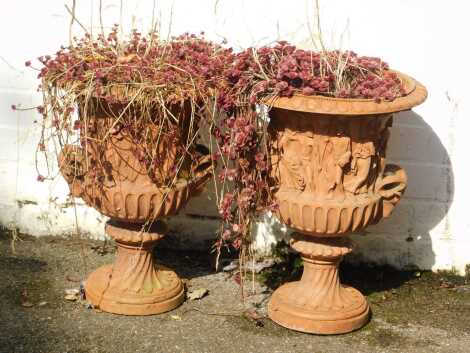 A pair of terracotta garden urns, each Neoclassically decorated with semi clad females and ram handles, 47cm high, 35cm wide. (AF)