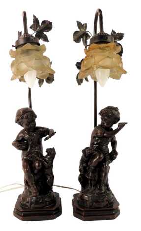 A pair of 20thC cast metal table lamps, each with a frosted floral shade, above a stand depicting a child feeding a cat, and a child beside a dog, 59cm high.