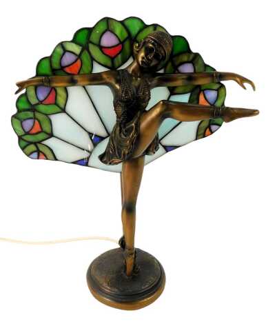 An Art Deco style table lamp, depicting a flapper girl dancing before a leaded stained glass fan shaped back, on a circular stepped base, 38cm high.WARNING! This lot contains untested or unsafe electrical items.  It is supplied for scrap or re-conditionin