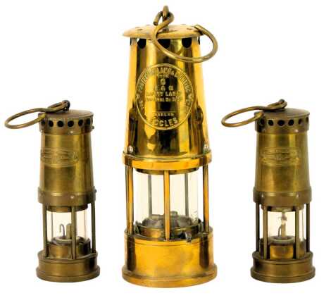 A Protector Lamp and Lighting Company brass miner's lamp, type 6, with ring handle, 23cm high, together with two miniature brass miner's lamps for E Thomas and Williams Ltd, Cambrian Works, 15cm high.