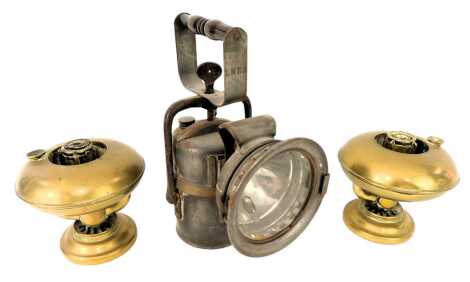 Two brass oil lamp bases, indistinctly stamped, 12cm high, together with an LNER railway lamp, with turned wooden handle, 26cm high.