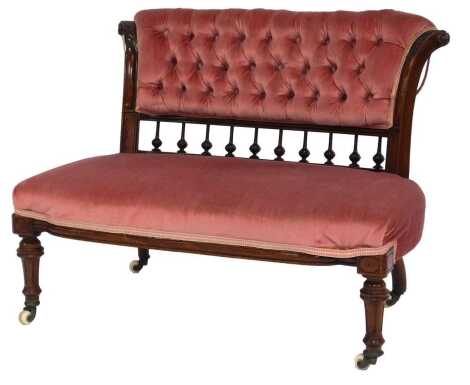 A Victorian walnut sofa, of small proportion, with a pink draylon button back, leaf and scroll carved end supports united by columns, with an overstuffed seat, on turned legs, on castors, 67cm high, 90cm wide,