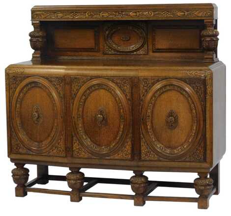 A 20thC oak sideboard, the raised back with carved decoration and central roundel supported by carved ball and cup supports, the bow fronted base with three carved cupboards decorated with floral and leaf motifs, the under tier united by carved ball and c