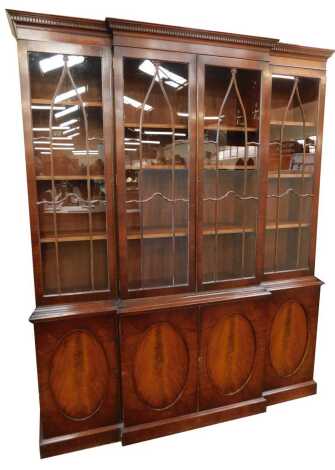 A 20thC mahogany breakfront bookcase in the Georgian style, the top with a dentil moulded edge, above four glazed doors, the base of four cupboards, each with oval roundel decoration, on a plinth base, 215cn high, 175cm wide, 44cm deep.