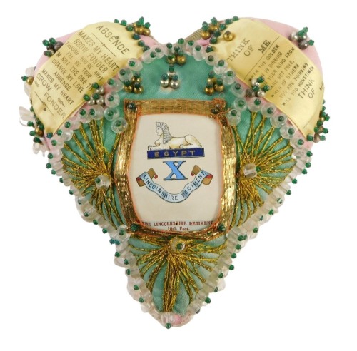 A Lincolnshire Regiment sweetheart heart shaped pin cushion, in pink silk with gold braid decoration, and regimental crest, printed ribbon text, 18cm.