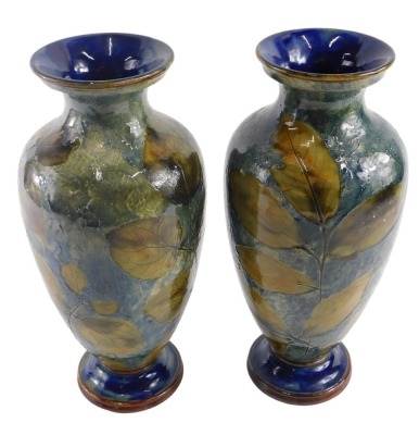 A pair of Royal Doulton stoneware Autumn Leaf pattern vases, of tapered ovoid form, with flared necks, and stepped feet, in brown and green glazes, with impressed leaf designs, with impressed marks and numbered 6768 to the bases, with incised initials LP,