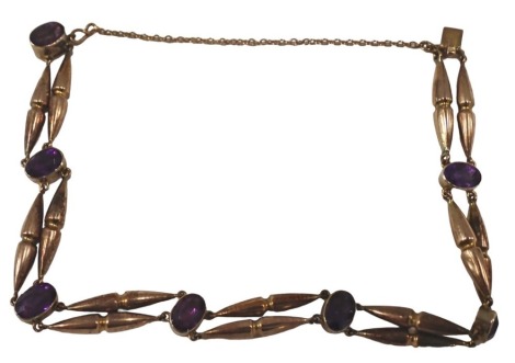 An Edwardian amethyst bracelet, the seven oval amethysts, in rub over setting, with bow shaped link chains, and safety chain, yellow metal stamped 9ct, 18cm long, 7.7g all in.