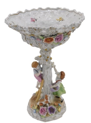 A 20thC German PMP porcelain figural table centre, in the form of an apple tree, with pierced basket top, encrusted with flowers and two children below picking apples, the rustic base with further encrusted flower decoration and a seated dog, with gilt hi