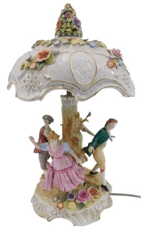 A 20thC German PMP porcelain figural table lamp, the pierced rococo style shade with cameos and encrusted flowers in polychrome enamels, supported on a tree trunk column, with dancing figures in traditional costume, the rustic rococo scrolling base with f