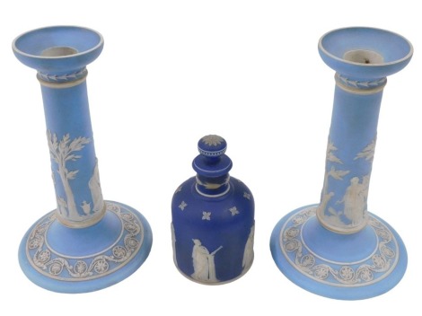 A pair of Wedgwood blue Jasperware candlesticks, and a scent bottle, the candlesticks on plain columns, and classical figures in relief, on tapered circular feet, 20cm high, the Wedgwood Jasperware scent bottle, knopped stopper, with classical figures in 