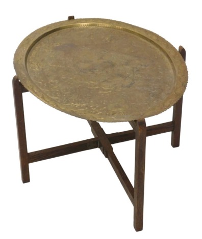 An Eastern hammered brass oval tray table, the brass tray with engine engraved scroll and floral decoration, 69cm x 54cm, on collapsable oak base.