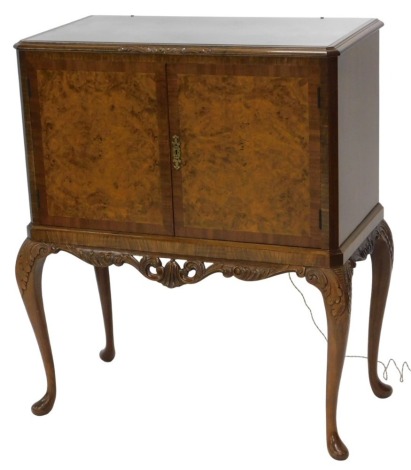 A reproduction figured walnut cocktail cabinet, with plate glass top and fitted interior enclosed by two doors with burr walnut veneer, with carved scroll apron below and carved cabriole legs, 109cm high, 95cm wide, 45cm deep. WARNING! This lot contains u