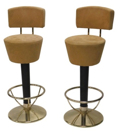 A pair of modern bar stools, with light brown suede upholstery, and metal tubular frames, on black pedestals, and tapering circular bases.