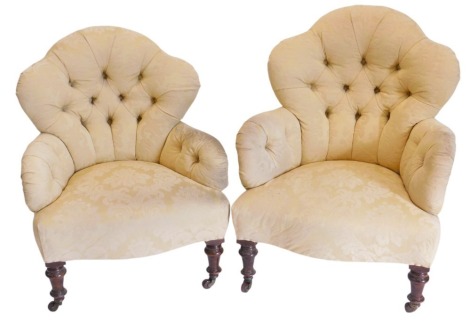 A pair of Victorian low seated button back upholstered arm chairs, in gold damask silk, on turned mahogany legs, and with pot castors.