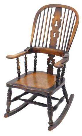 A Victorian elm and beech rocking chair, with high comb back and pierced splat, scrolling arms, and turned supports below, with shaped seat, and turned legs and stretchers.