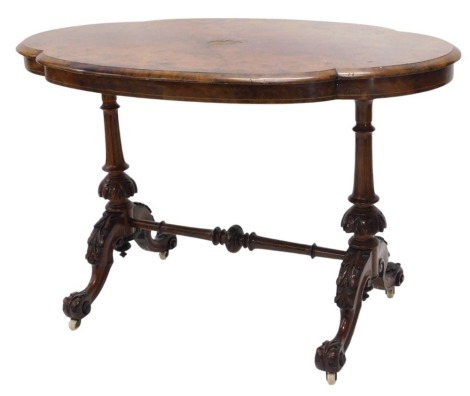 A Victorian inlaid and figured walnut centre table, of shaped oval design, with shallow frieze, on two turned and tapered carved pillar supports and with scrolling legs having carved foliate knees and pot castors, 111cm x 70cm.