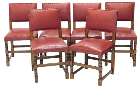 A set of six oak Carolean style dining chairs, with studded red vinyl leather backs and over upholstered seats.