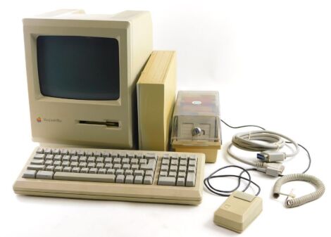 An Apple Macintosh Plus computer monitor, with exterior hard drive, keyboard, cables, mouse and floppy discs.